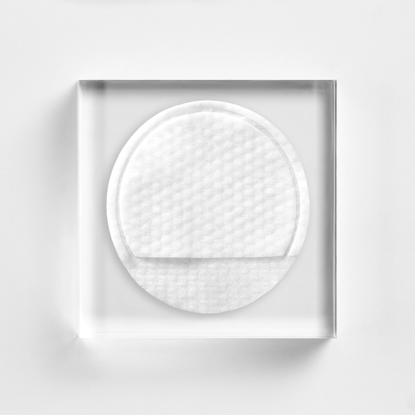 NEOVA 5- Second Daily Peel - texture image: an embossed round, white cotton pad on clear acrylic, highlighting its gently textured exfoliating surface.
