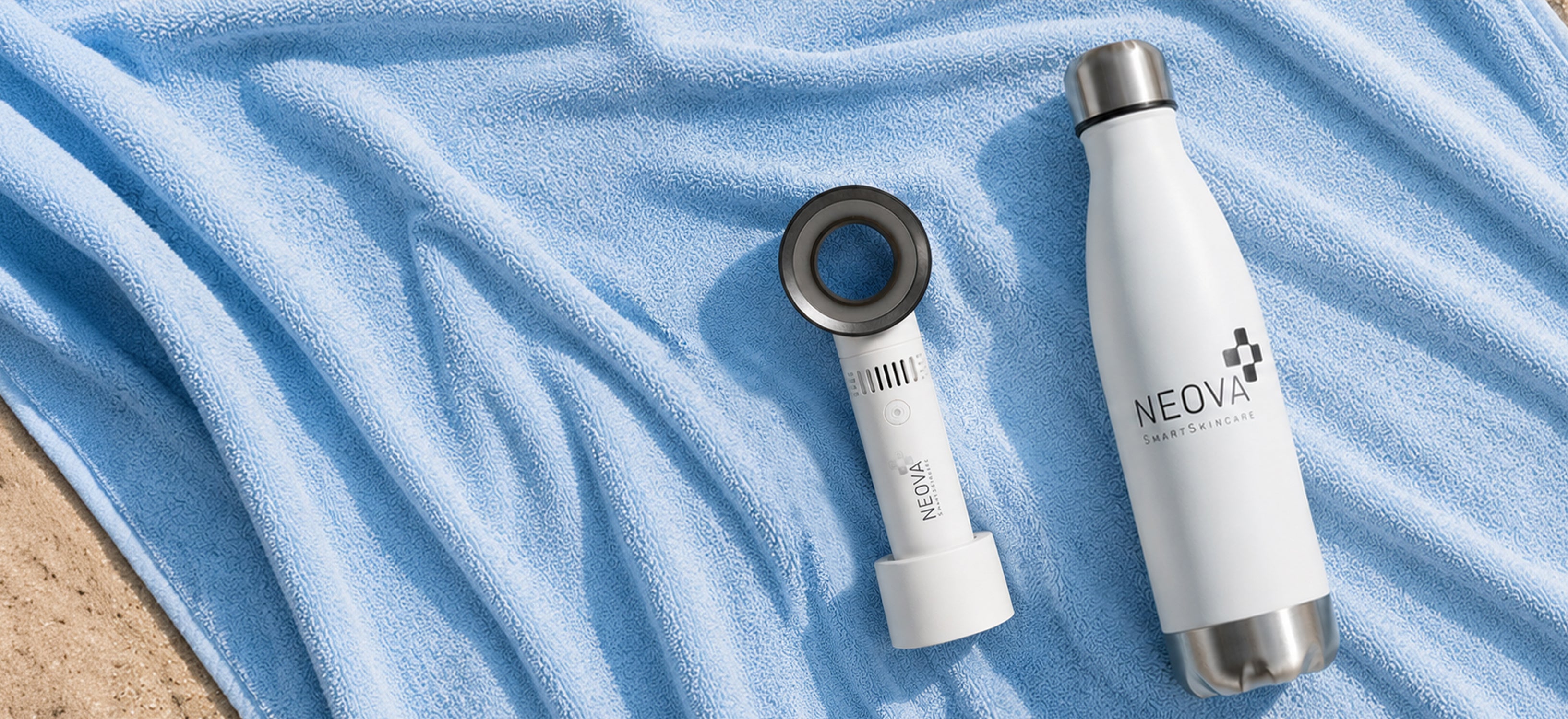 NEOVA - bottle and fan gwp - A white insulated water bottle and a white handheld fan with a circular lens-like top are arranged on a light blue towel on a sandy beach. The bottle and fan show the brand name NEOVA.