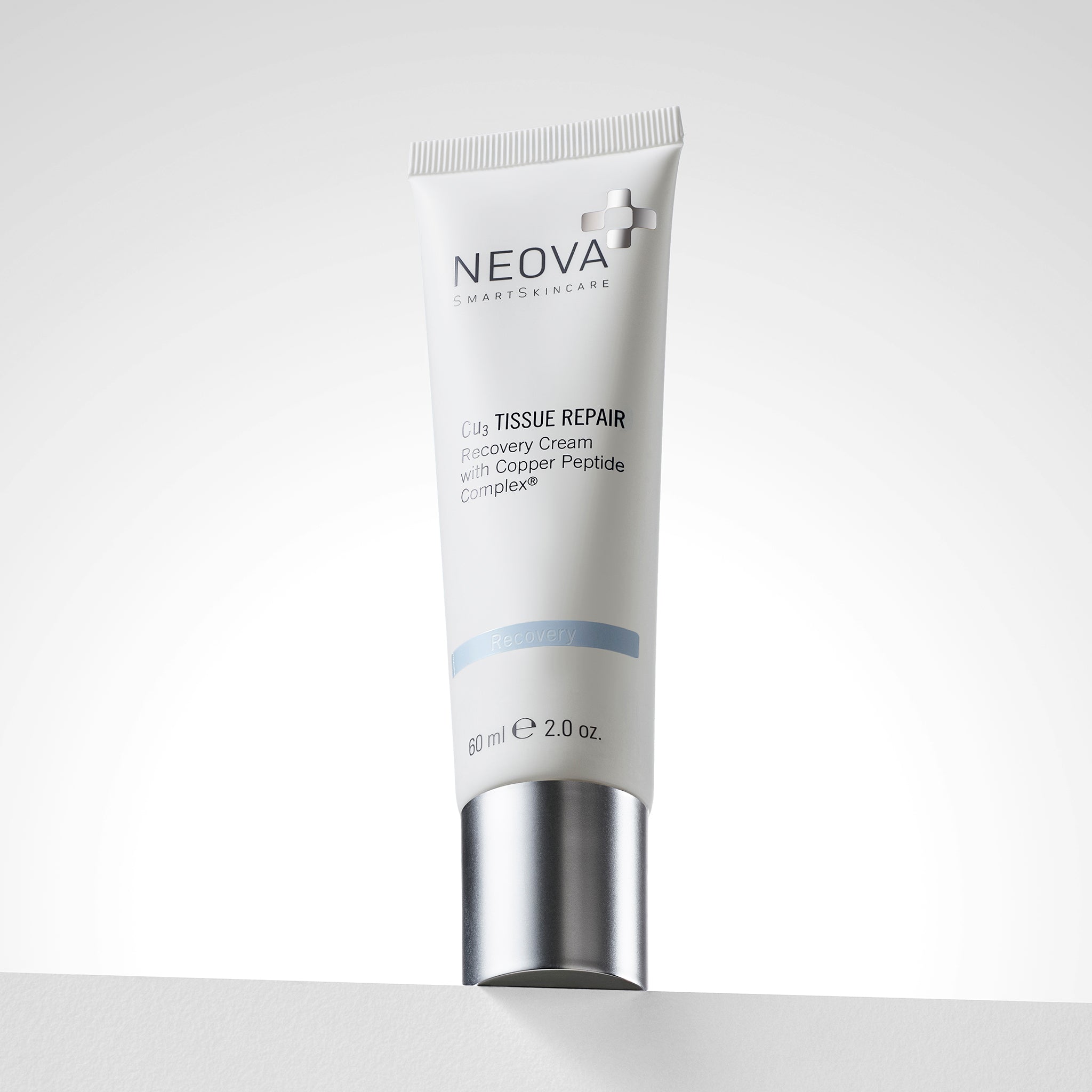 NEOVA Cu3 Tissue Repair in a white squeeze tube. The front label identifies it as a "Recovery Cream with Copper Peptide Complex" and features a light blue "Recovery" banner. The tube is shown standing upright on its wide, brushed silver screwcap and contains 2.0 oz. (60 ml). It is positioned on a white ledge against a bright, clean background.
