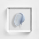 NEOVA Illuminating Eye Serum's smooth, glossy texture with a soft, gel-cream consistency, spread in an organic shape on a clear acrylic plate against a bright white background. The top-down macro view highlights the product's hydration and luminosity in a clinical skincare aesthetic.