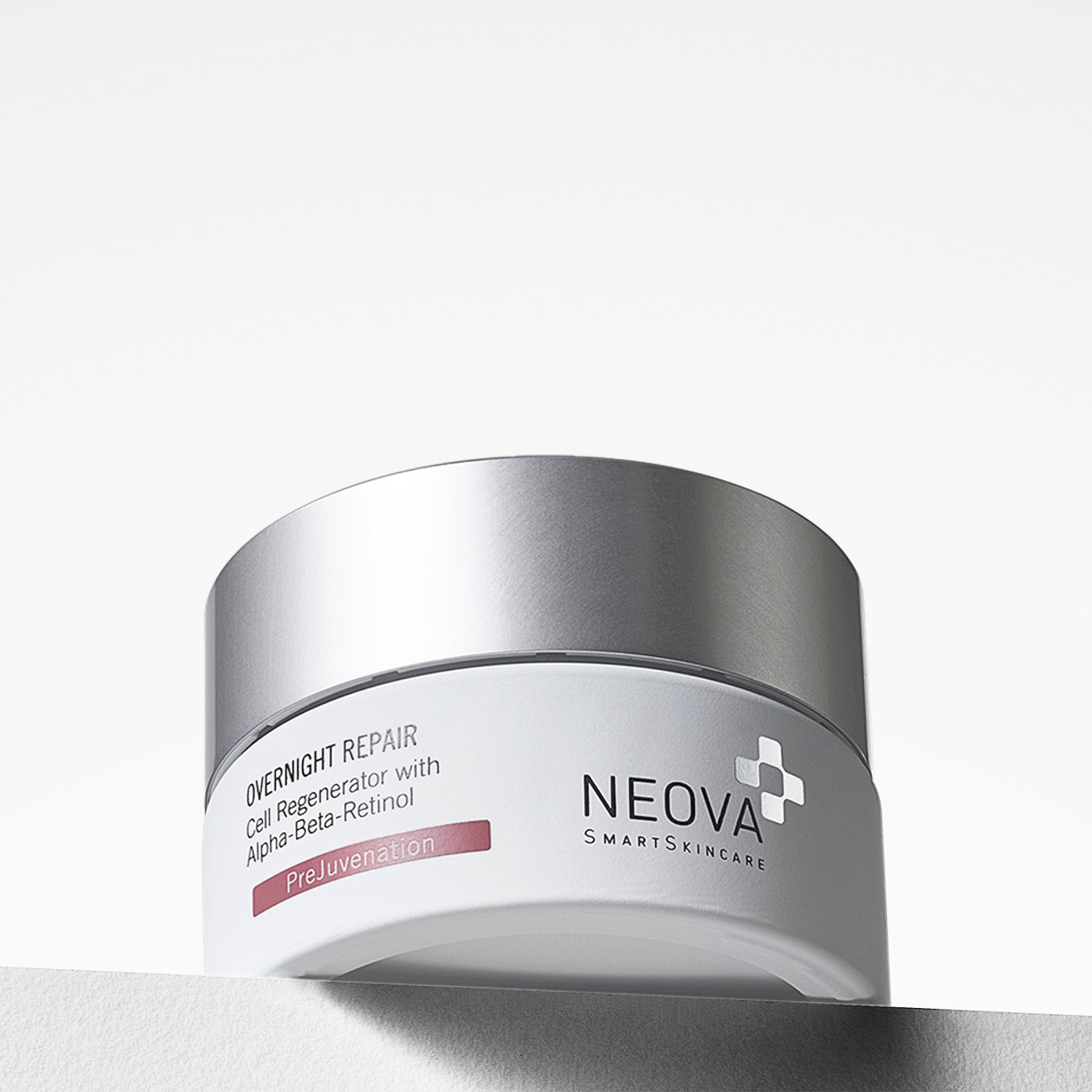 NEOVA Overnight Repair in a white cosmetic jar. The front label specifies it is a "Cell Regenerator with Alpha-Beta-Retinol and features a red "PreJuvenation" banner. The jar is topped with a flat, brushed silver screw-cap and sits on a clean white surface against a bright, minimalist background.