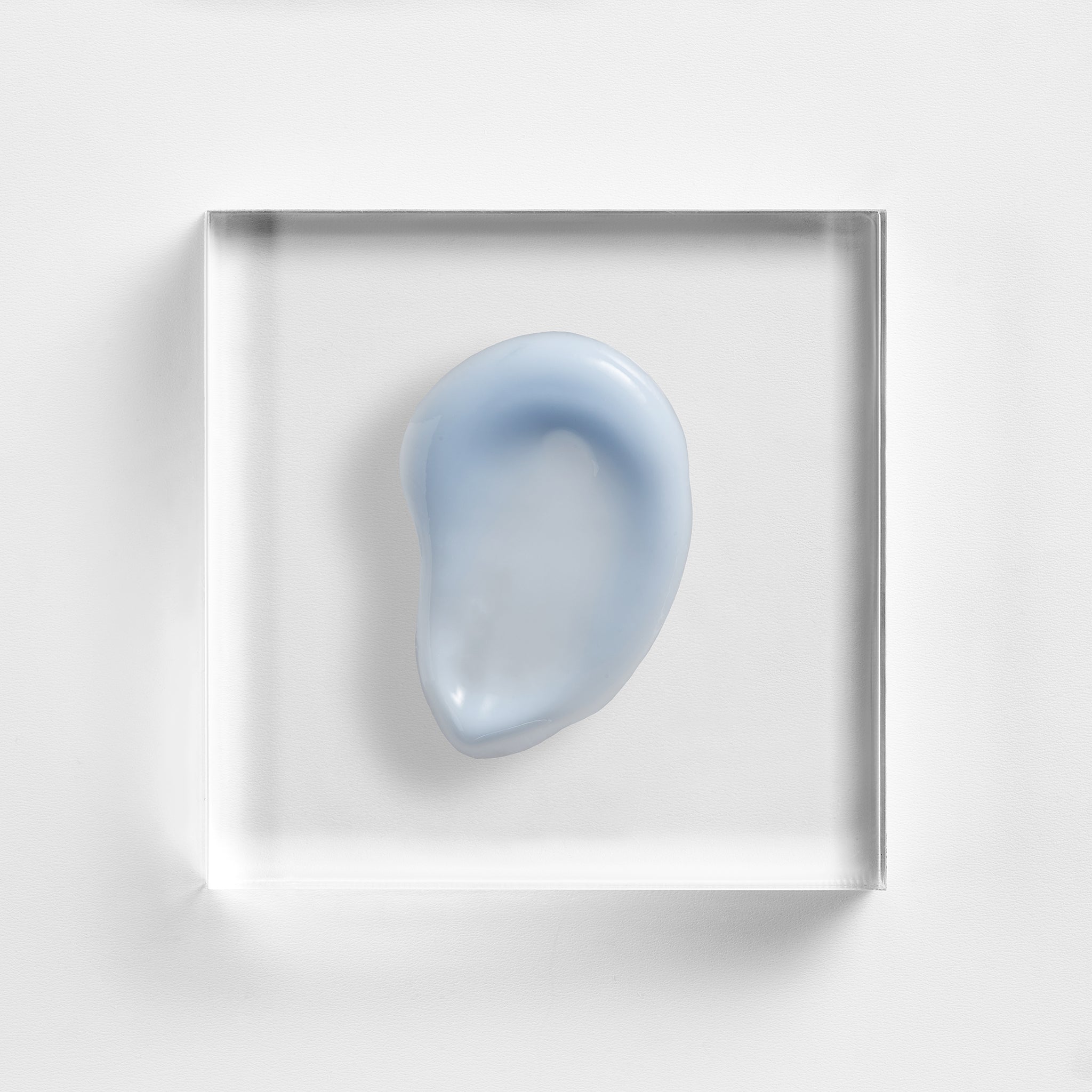 NEOVA Super Eye Lift Serum on a clear acrylic square. The top-down, square macro view shows the serum is a smooth, opaque light blue-white cream with a slight glossy finish and a lightweight, refined consistency. It is centered and brightly lit against a textured white background, highlighting its silky texture.