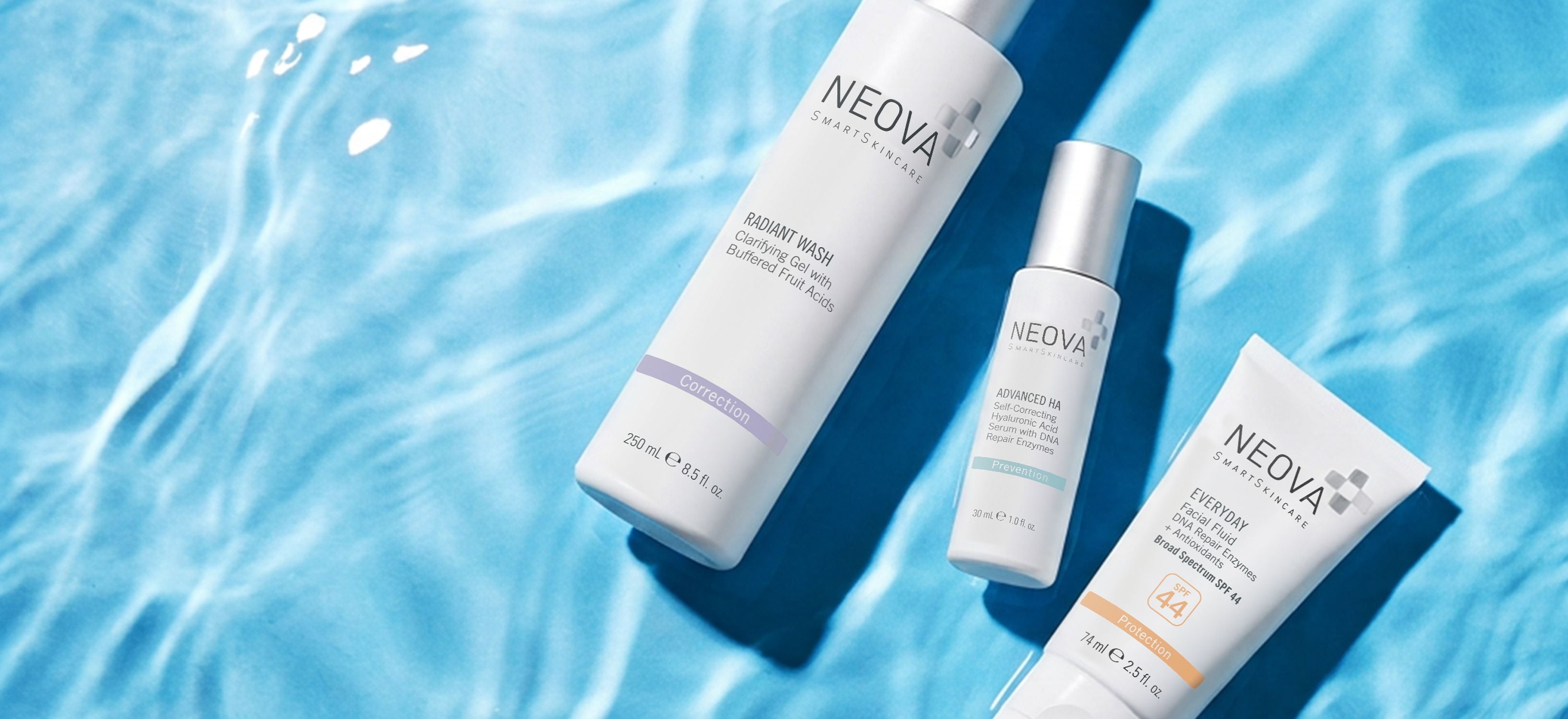 NEOVA - travel essentials - Three NEOVA Skincare products from a travel routine arranged diagonally on a blue water-textured background: a large Radiant Wash bottle, a smaller Advanced HA hyaluronic acid serum bottle, and a tube of Everyday SPF 44.