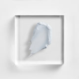 NEOVA Ultimate Redness Relief on a clear acrylic square. The top-down macro view shows the product is a smooth, opaque cream with a distinct pale seafoam-green tint designed to neutralize redness. It has a rich, velvety consistency and is centered against a textured white background with soft, clean lighting.