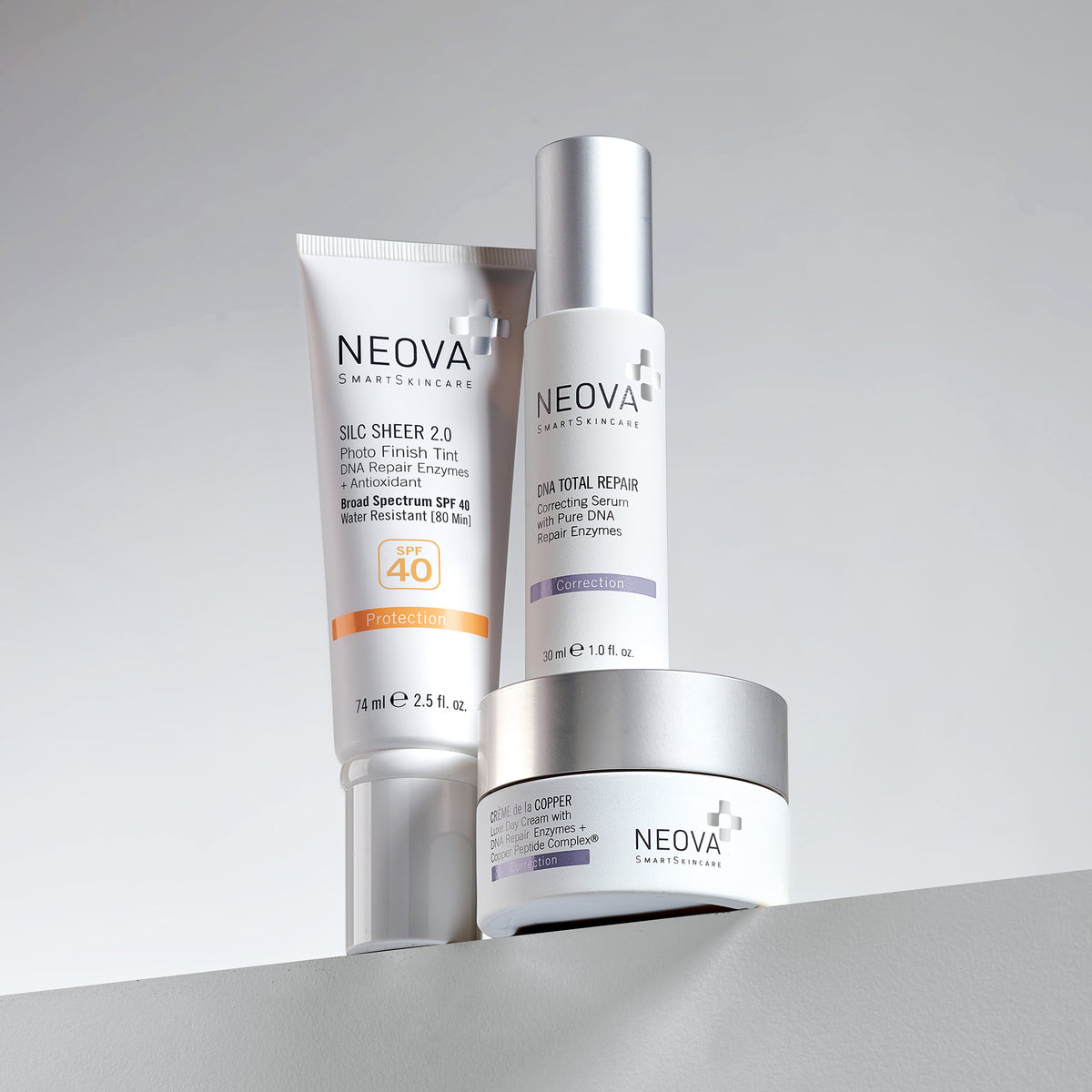 NEOVA SmartSkincare best sellers: Silc Sheer 2.0 Photo Finish Tint SPF 40, DNA Total Repair Correcting Serum, and Crème de la COPPER in a jar. These professional-grade formulas are shown together in a minimalist clinical display on a ledge to represent a complete daily regimen of protection, DNA repair, and copper peptide restoration.