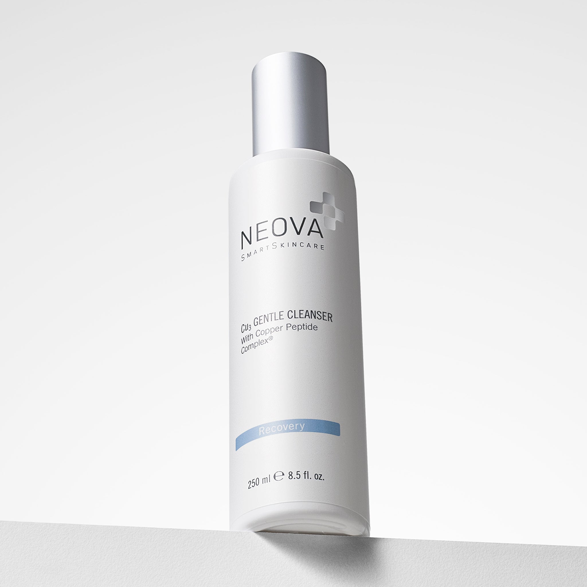 NEOVA Cu3 Gentle Cleanser containing a Copper Peptide Complex® formula. The front label of the tall, white cylindrical bottle categorizes it under a light blue "Recovery" banner. The bottle features a brushed silver cap and contains 8.5 fl. oz. (250 ml), shown from a low angle resting on a white surface against a bright, minimalist background.