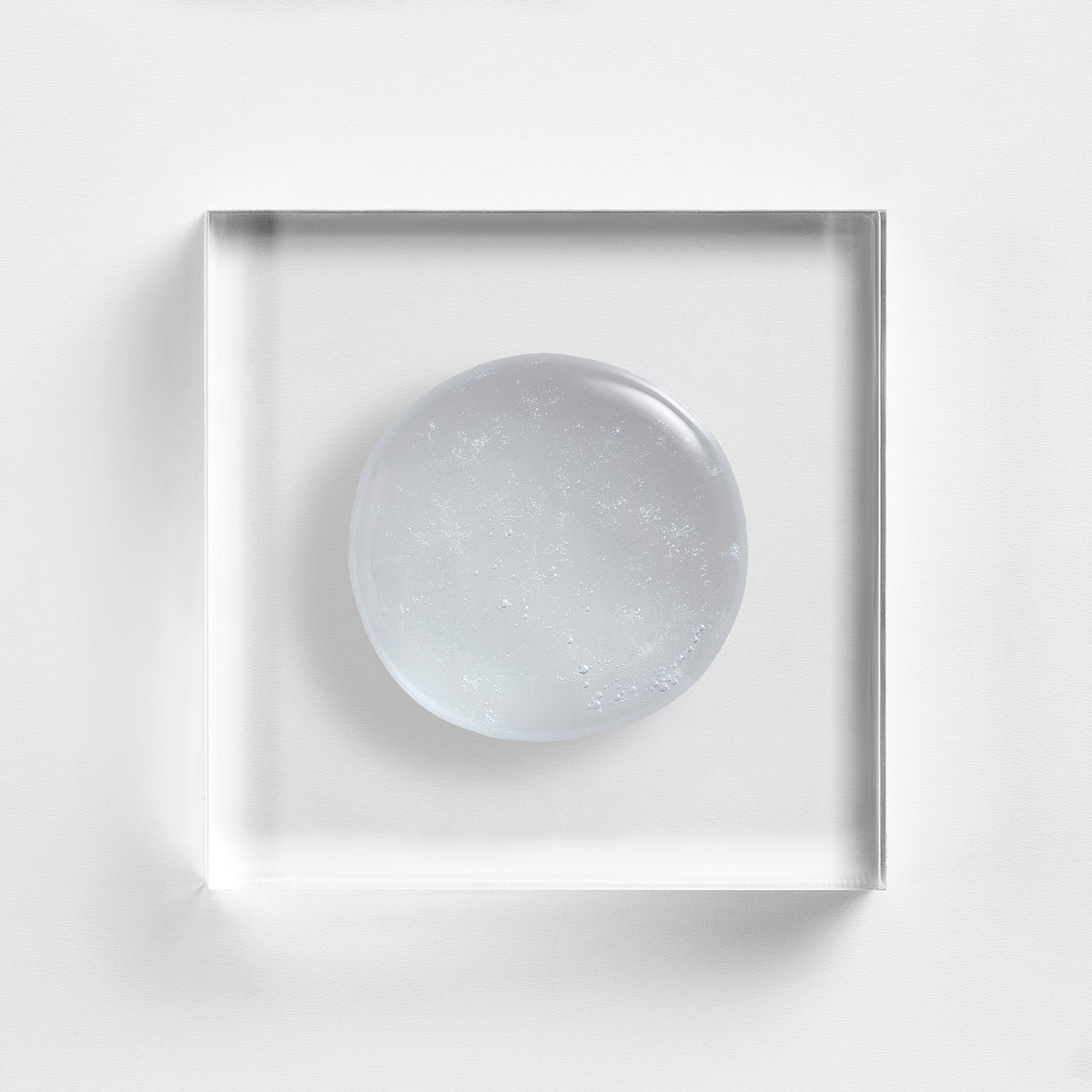 NEOVA Cu3 Gentle Cleanser on a clear acrylic block. The top-down macro view shows the facial cleanser is a transparent, colorless gel with many tiny, suspended oxygen bubbles throughout, giving it a fresh and aerated appearance.