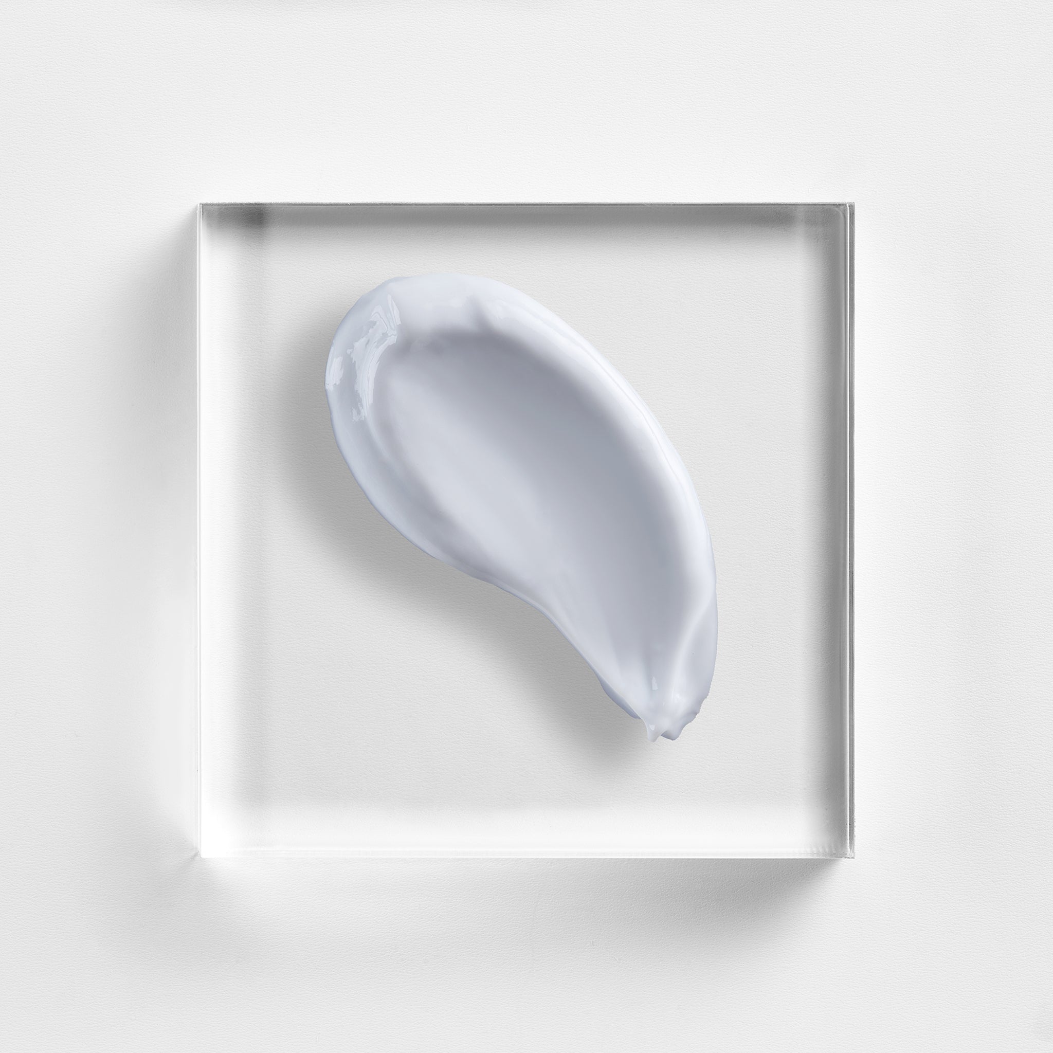 NEOVA Daily Moisture cream on a clear acrylic block. The top-down, macro composition shows the cream is a clean, opaque white with a rich, velvety appearance and a slight glossy sheen. It is centered against a minimalist, white background, highlighting its thick and hydrating consistency.