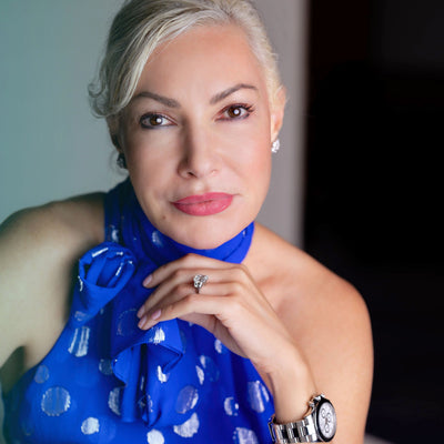 NEOVA - Woman wearing a blue dress with white polka dots, sitting indoors. The woman is Dr. Ivona Percec, a board-certified dermatologist on NEOVA's Medical Advisory Council
