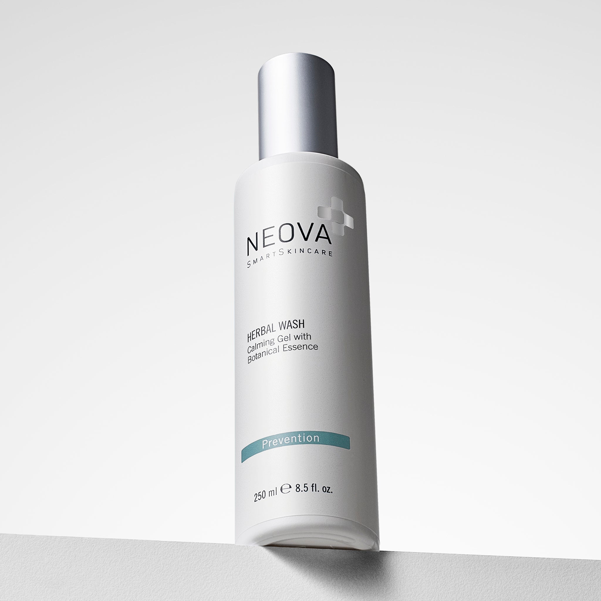 NEOVA Herbal Wash, a gentle gel cleanser with botanical extracts, in a tall, white cylindrical bottle. The front label categorizes it under a blue "Prevention" banner. The bottle features a brushed silver cap and contains 8.5 fl. oz. (250 ml). It is shown standing on a white ledge against a clean, minimalist background with soft lighting.