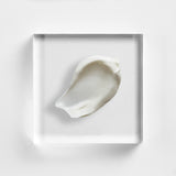 NEOVA Multi-Active Day Cream on a clear acrylic block. The top-down, square macro view shows the cream is a clean, opaque white with a firm, rich consistency that holds its shape. It is centered and brightly lit against a textured white background, highlighting the moisturizer's smooth and nourishing texture.