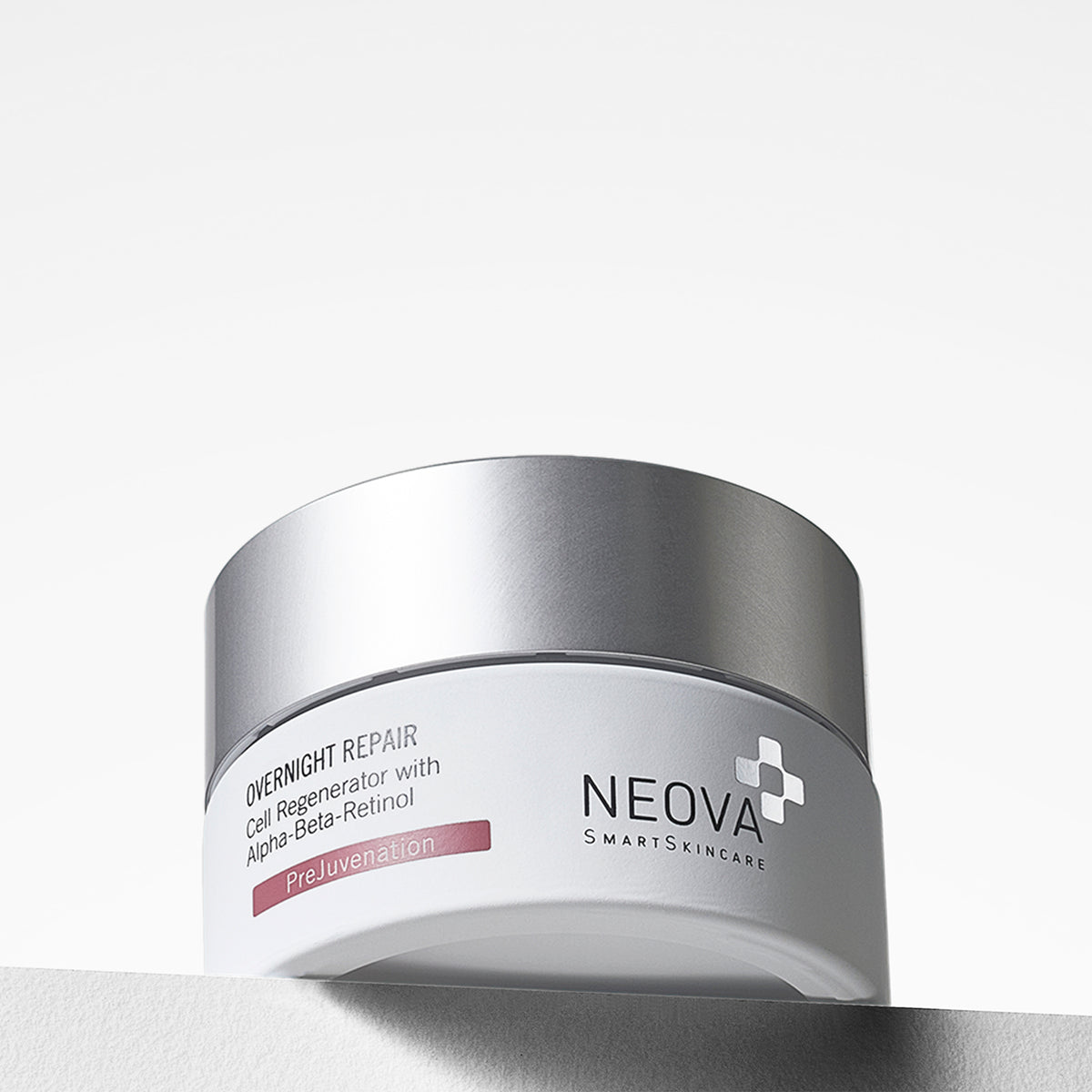 NEOVA Overnight Repair in a white cosmetic jar. The front label specifies it is a "Cell Regenerator with Alpha-Beta-Retinol and features a red "PreJuvenation" banner. The jar is topped with a flat, brushed silver screw-cap and sits on a clean white surface against a bright, minimalist background.