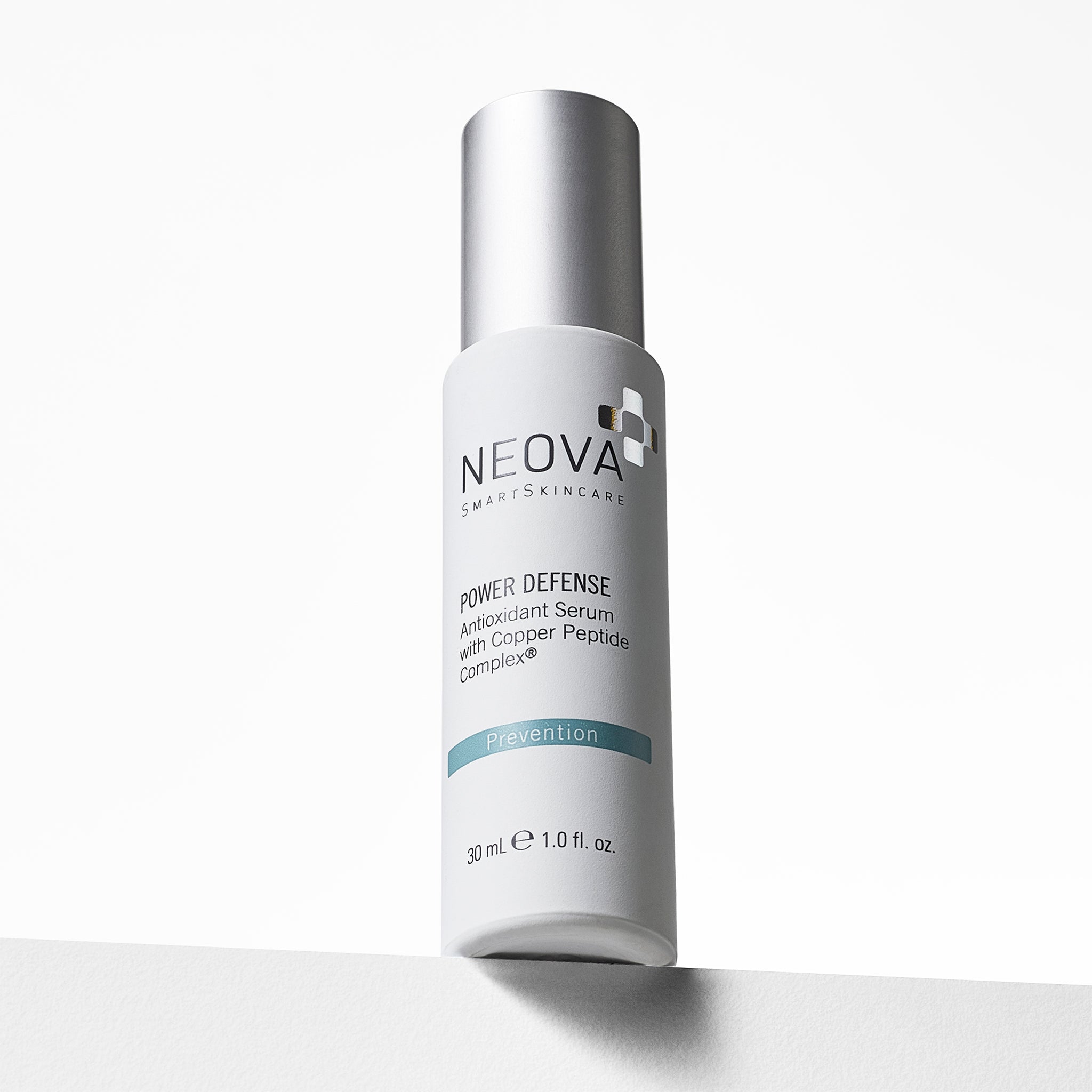 NEOVA Power Defense in awhite cylindrical bottle. The front label describes it as an "Antioxidant Serum with Copper Peptide Complex®, categorizing it under a blue "Prevention" banner. The bottle features a brushed silver pump cap and contains 1.0 fl. oz. (30 ml). It is shown from a low angle, standing on a white ledge against a clean, bright minimalist background.