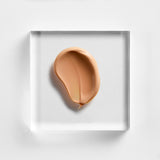 NEOVA Silc Sheer 2.0 nude-beige cream sunscreen centered on a clear acrylic square. The top-down macro view of the sun block's texture appears rich yet lightweight, and has a subtle gloss, suggesting a creamy consistency. The entire composition is set against a clean, textured white background.